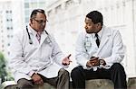 Black and Hispanic male doctors discussing a case in a hospital hallway.