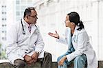 Hispanic man and Asian woman doctors conferring over a case in a hospital.