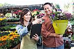 Caucasian man buying plants with a credit card at a nursery owned by a Caucasian woman using a credit card reader on a notebook computer