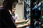 Caucasian woman and man technicians working on CAT 5 cables in a large computer server farm.