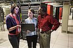 Mixed race group of technicians doing diagnostic tests on servers in a large server farm.