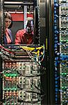 Caucasian woman and black man technicians running diagnostic tests on servers in a large computer server farm.