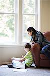 Young boy doing home work with his mother sitting close by.