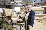 Caucasian senior male upholsterer working on a chair in his garage shop.