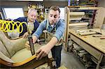 Young Caucasian man learning the art of upholstery from a senior male upholsterer.