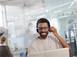 Smiling creative businessman with headphones working at laptop in office