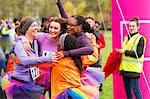 Enthusiastic female runners in tutus hugging at finish line, celebrating