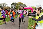 Female runner in tutu reaching for water during charity run in park