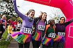 Enthusiastic female runners in tutus cheering, crossing finish line at charity run, celebrating