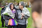 Happy couple runners wrapped in thermal blanket at charity run in park