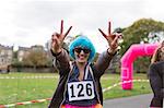 Portrait enthusiastic female runner in wig gesturing peace sign at charity run in park