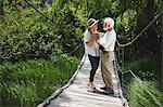 Romantic active senior couple holding hands on idyllic footbridge