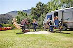 Active senior friends relaxing outside camper van at sunny summer campsite