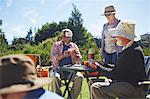 Playful active senior friends playing cards at sunny summer campsite