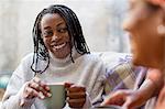 Enthusiastic, smiling woman listening to friend and drinking coffee