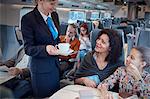 Attendant serving coffee to mother with daughter on passenger train