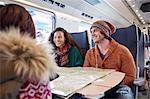 Smiling young friends planning with map on passenger train