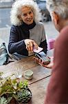 Woman using smart phone contactless payment at cafe