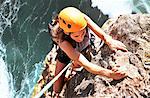 Focused female rock climber hanging from rock above ocean