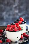 Fresh ripe blueberry and raspberry in enamel mugs