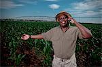 Black farmer stands smiling in a crop field with irrigation systems in the background