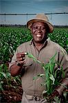 Black farmer stands holding his crops and smiling in a crop field