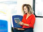 Mid adult woman on train, using digital tablet