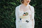 Bride with wedding cake, hedge in background