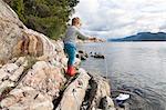 Boy standing on rock by fjord playing with toy boat, Aure, More og Romsdal, Norway