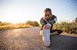 Young woman exercising in rural setting, stretching leg