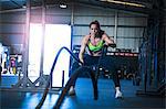 Woman exercising in gym, using battle ropes