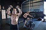 Two men exercising in gymnasium, using kettlebells and using air resistance exercise bike