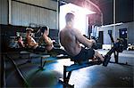 Group of people exercising in gymnasium, using rowing machines, rear view