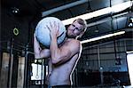 Man exercising in gymnasium, using atlas stone