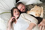 Pregnant woman lying with partner on bed, dog lying on bed beside them, elevated view