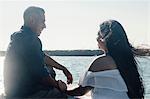 Couple sitting on coastal rocks, holding hands, smiling