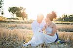 Heterosexual couple sitting in field, face to face, smiling