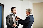 Senior businessman fastening colleague's tie in office