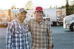 A Caucasian man and a black man truck driving team together in a truck stop parking lot.