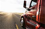 Close up side view looking forward of a  commercial truck on a highway at sunset.