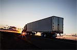 Silhouette of a  commercial truck driving on a highway at sunset.