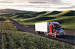 A commercial truck driving through farmlands in eastern Washington, USA at sunset.