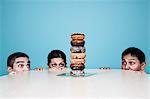 Business people hiding behind a table with a stack of doughnuts on it.