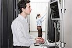 A male computer technician standing in an aisle of racks of servers in a computer server farm