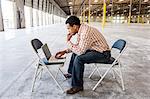 Black man working on lap top computer in front of loading dock doors in a new warehouse.