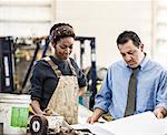 Hispanic man manager and black woman factory worker going over project plans in a sheet metal factory.