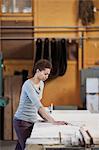 Black woman factory worker measuring wood at a work station in a woodworking factory.