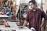 Caucasian man factory worker working on a lap top computer at a work station in a woodworking factory.