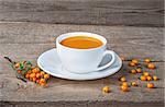 Seabuckthorn juice and berries on wooden table. Sea-buckthorn juice in a white cup on the table.