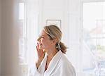 Smiling mature woman applying moisturizer to face in bathroom